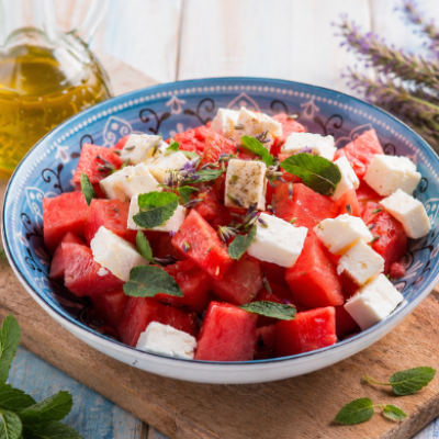 Ensalada de sandía y queso feta servida en un cuenco de inspiración mediterránea, acompañada de hojas de menta fresca y aceite de oliva virgen extra sobre una mesa de verano.