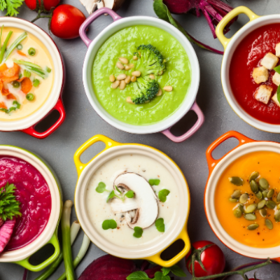 Seis cremas de verduras de distintos colores servidas en pequeños cuencos, acompañadas de vegetales frescos, semillas, hierbas y setas.