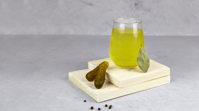 Vaso con jugo de pepinillos y dos pepinillos